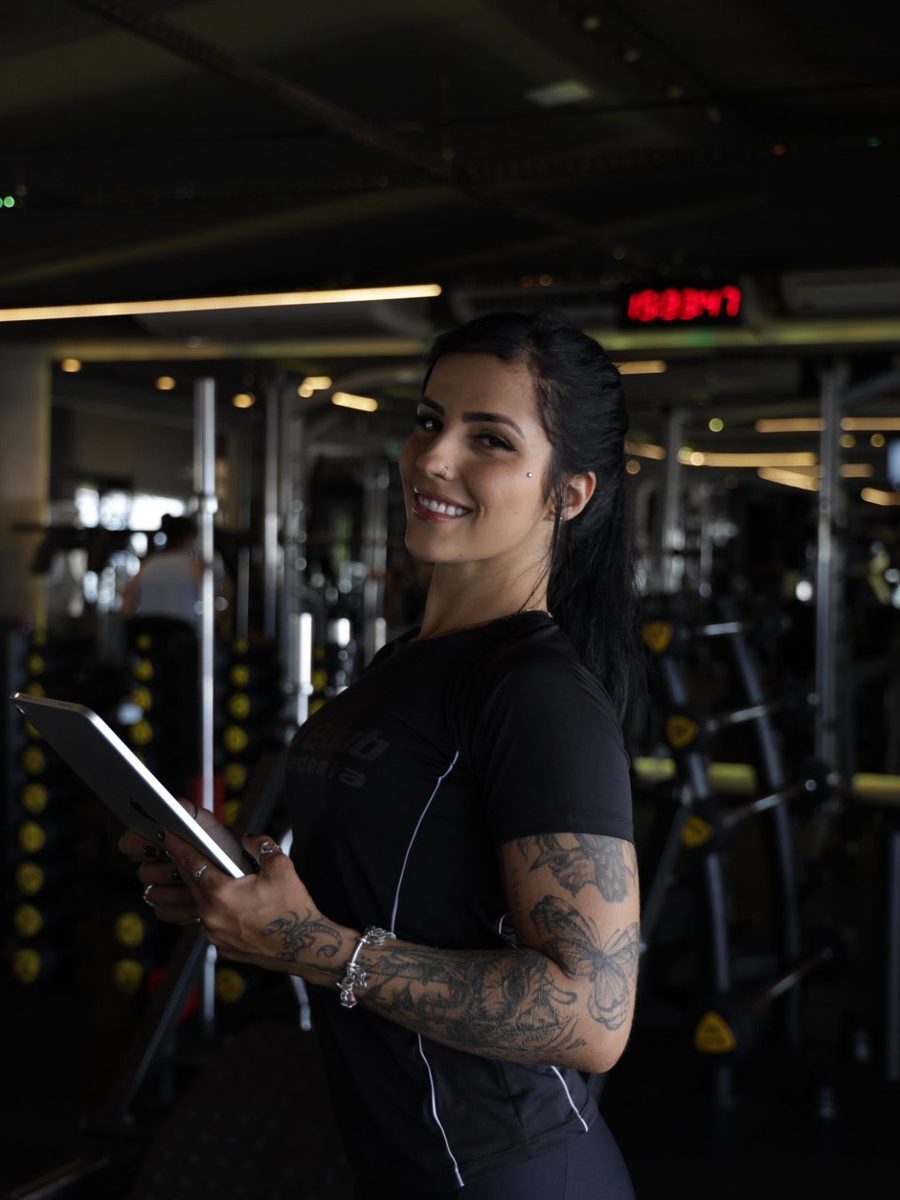Nathâny Lisita sorrindo, segurando um tablet no ambiente da academia Life Club em Rio Verde, GO